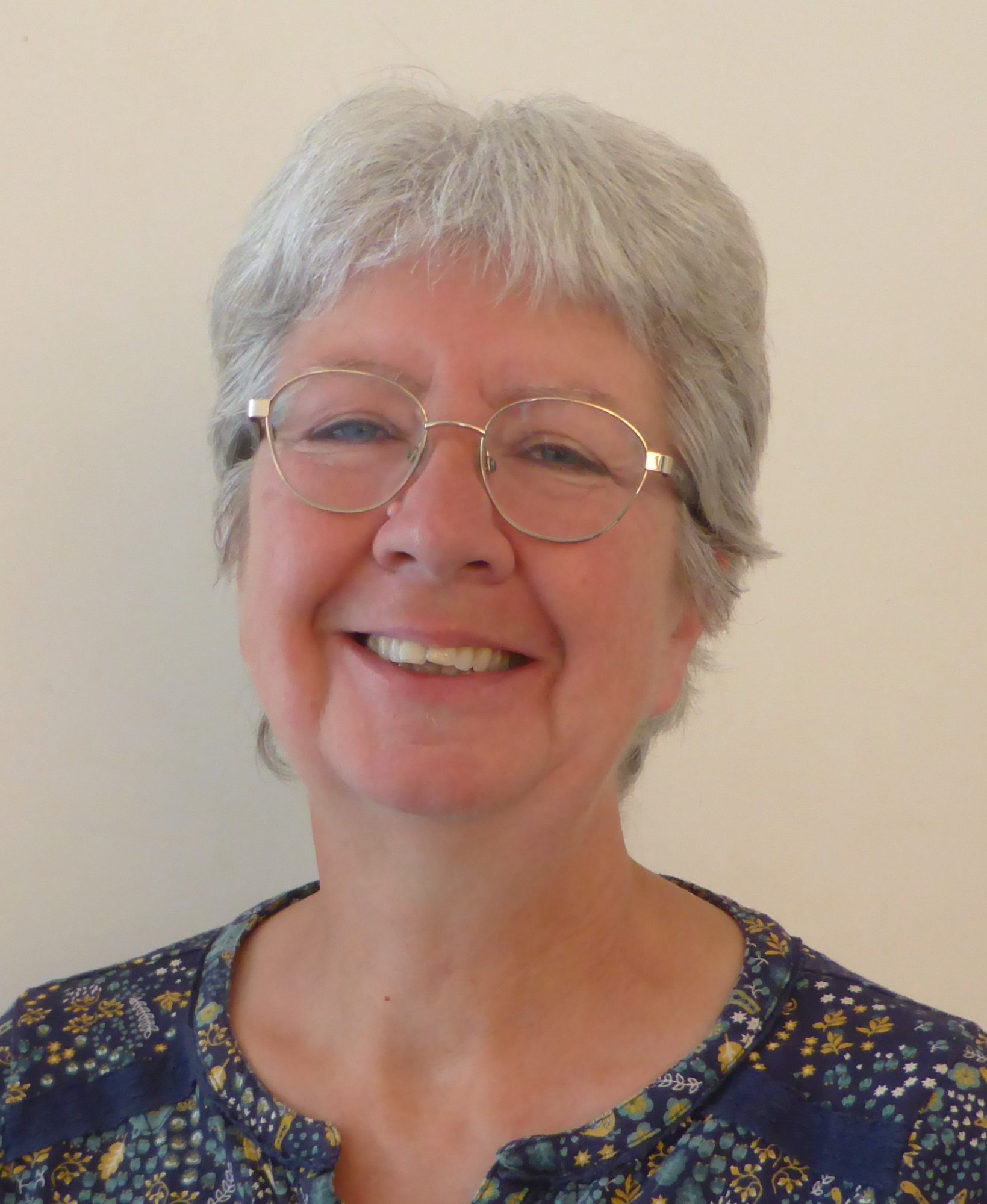 Helen - a smiling older woman with short grey hair, wearing glasses and a patterned top.