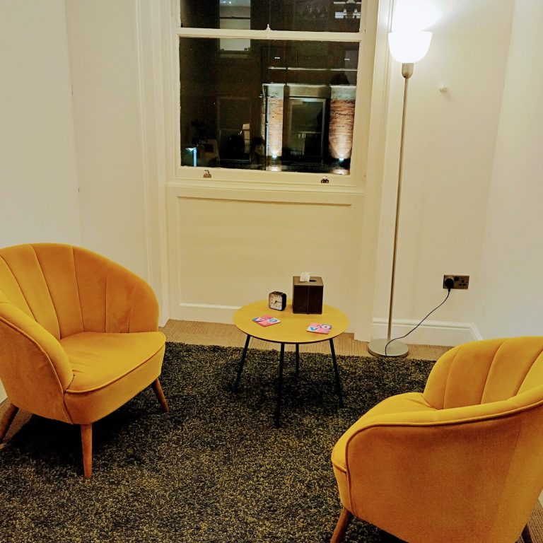 Two yellow armchairs beside a small table, situated on a carpet in a well-lit room.